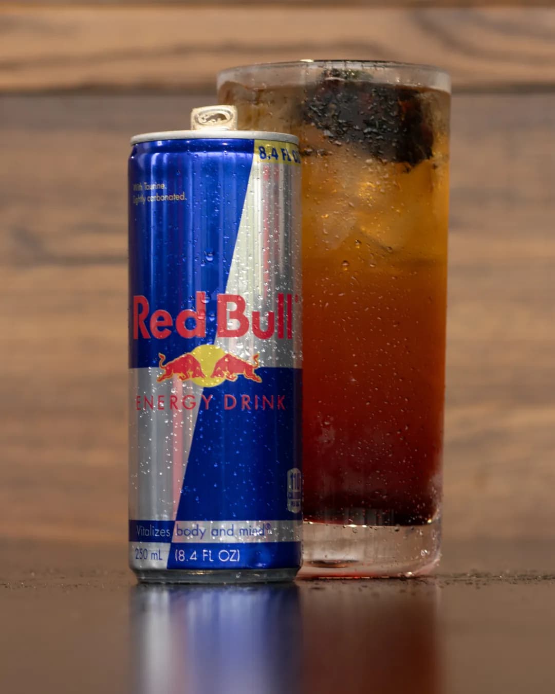 A tall Blackberry Bramble Red Bull Infusion over ice beside a can of Red Bull Energy Drink