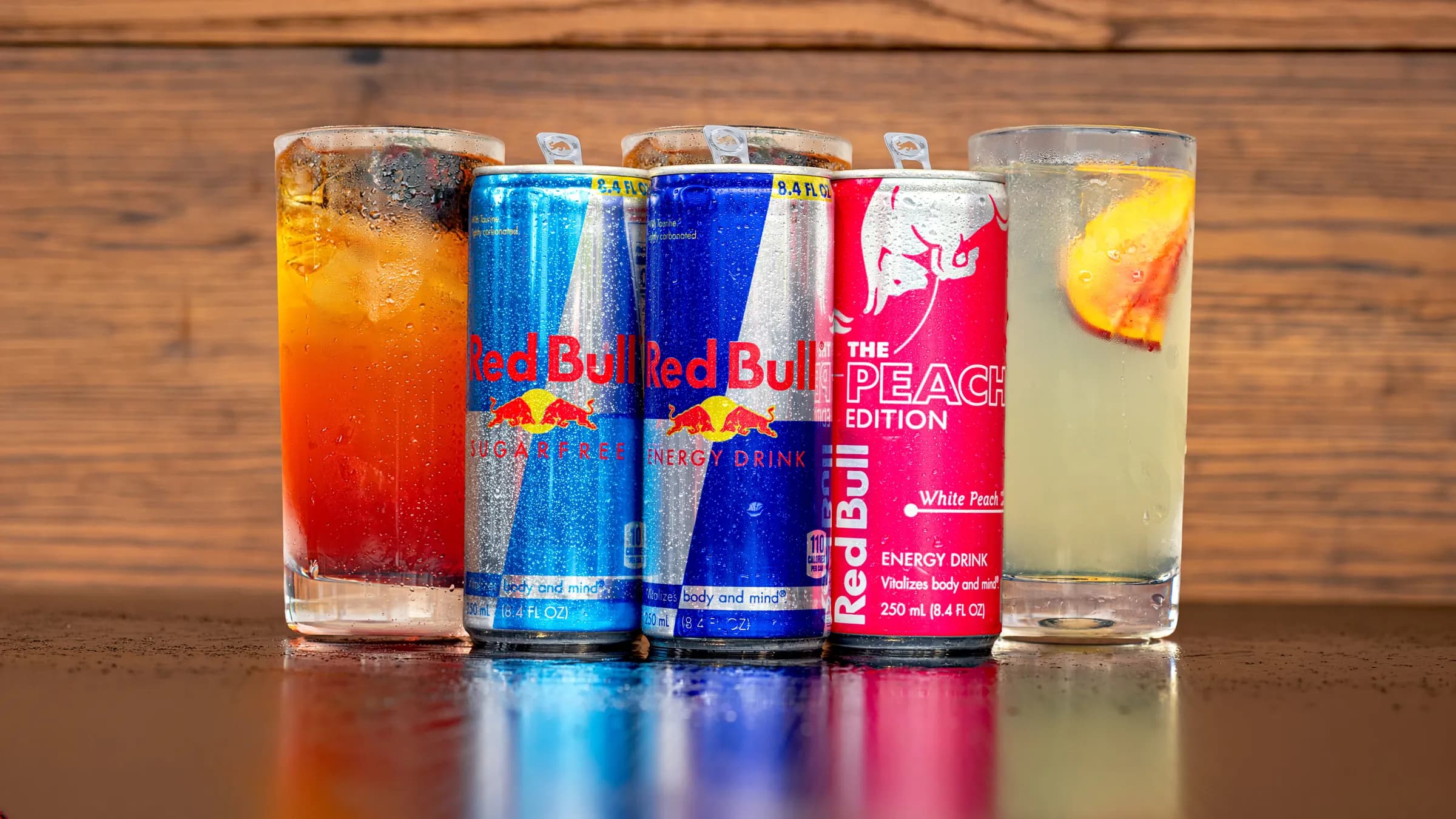 Cans of Red Bull Sugarfree, Red Bull Energy Drink and Red Bull Peach Edition between a Blackberry Bramble Infusion and a White Peach & Honey Infusion, served tall over ice.